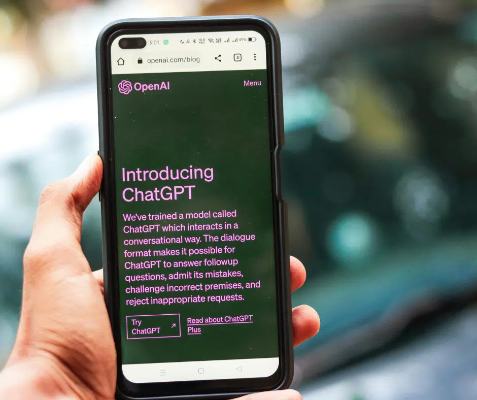 Hand hält ein Smartphone, auf dessen Display die OpenAI-Website mit der Vorstellung von ChatGPT angezeigt wird.