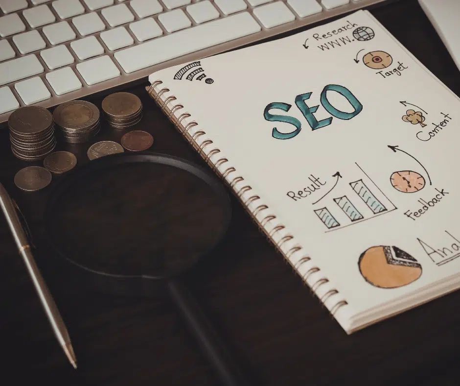Notizbuch mit handgezeichneten SEO-Notizen, daneben ein Stapel Münzen, eine Lupe und eine Tastatur.
