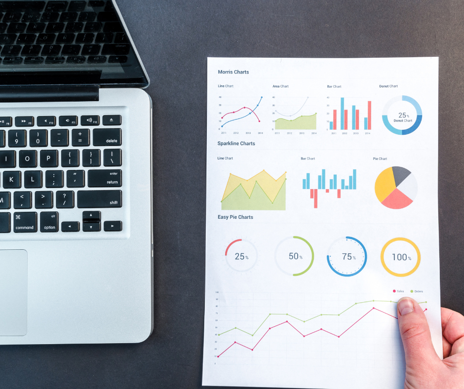 Laptop neben einem Blatt Papier mit farbigen Diagrammen – darunter Linien-, Balken- und Kreisdiagramme, die unterschiedliche Datenverläufe darstellen; symbolisch für die zeitlich gestaffelte Wirkung von SEO-Strategien.